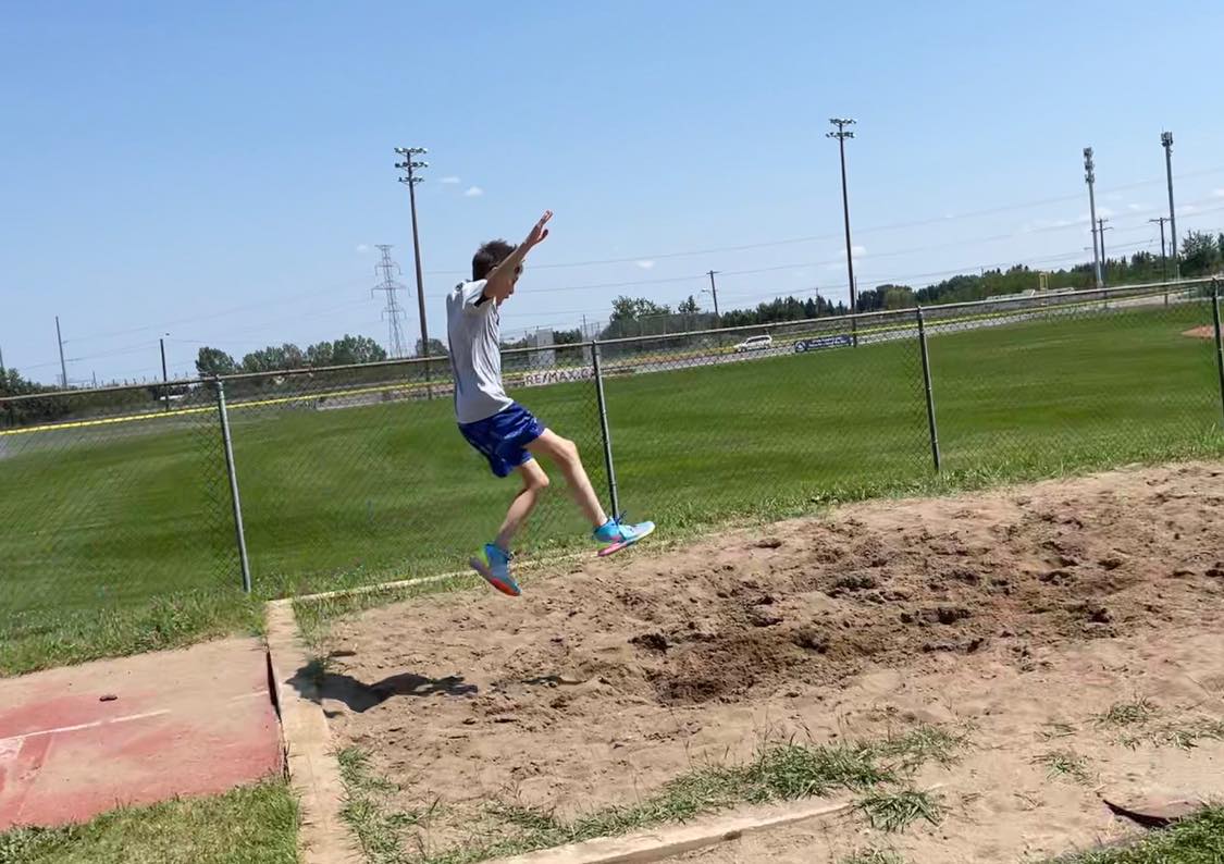 A child jumps in the long jump pit at a summer track and field day camp in Calgary.