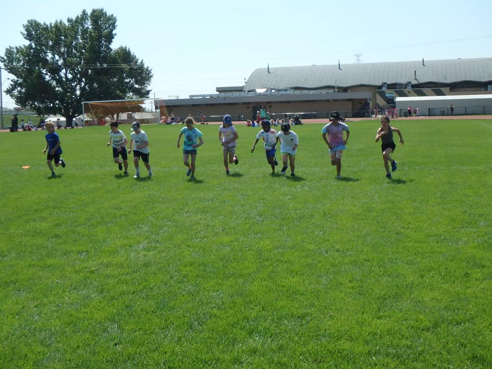 Kids running through the infield at a summer track and field day camp in Calgary.