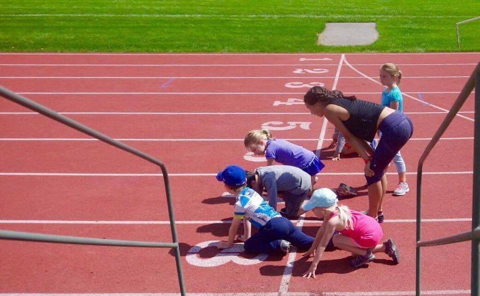 A coach at a summer track and field day camp in Calgary coaches children lining up on a running track.